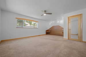 Spacious room featuring neutral carpeting, a built-in wood headboard with integrated shelving, track lighting, and a ceiling fan
