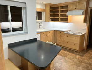 Kitchen featuring light wood finish cabinets, backsplash, black electric cooktop, and dark countertops