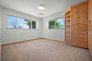 Room featuring built-in wood cabinetry with shelving and drawers, neutral carpet, and white walls