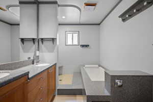 Bathroom featuring a deep soaking tub, double vanity with stone-finish countertops, wood-finish cabinetry, and recessed lighting