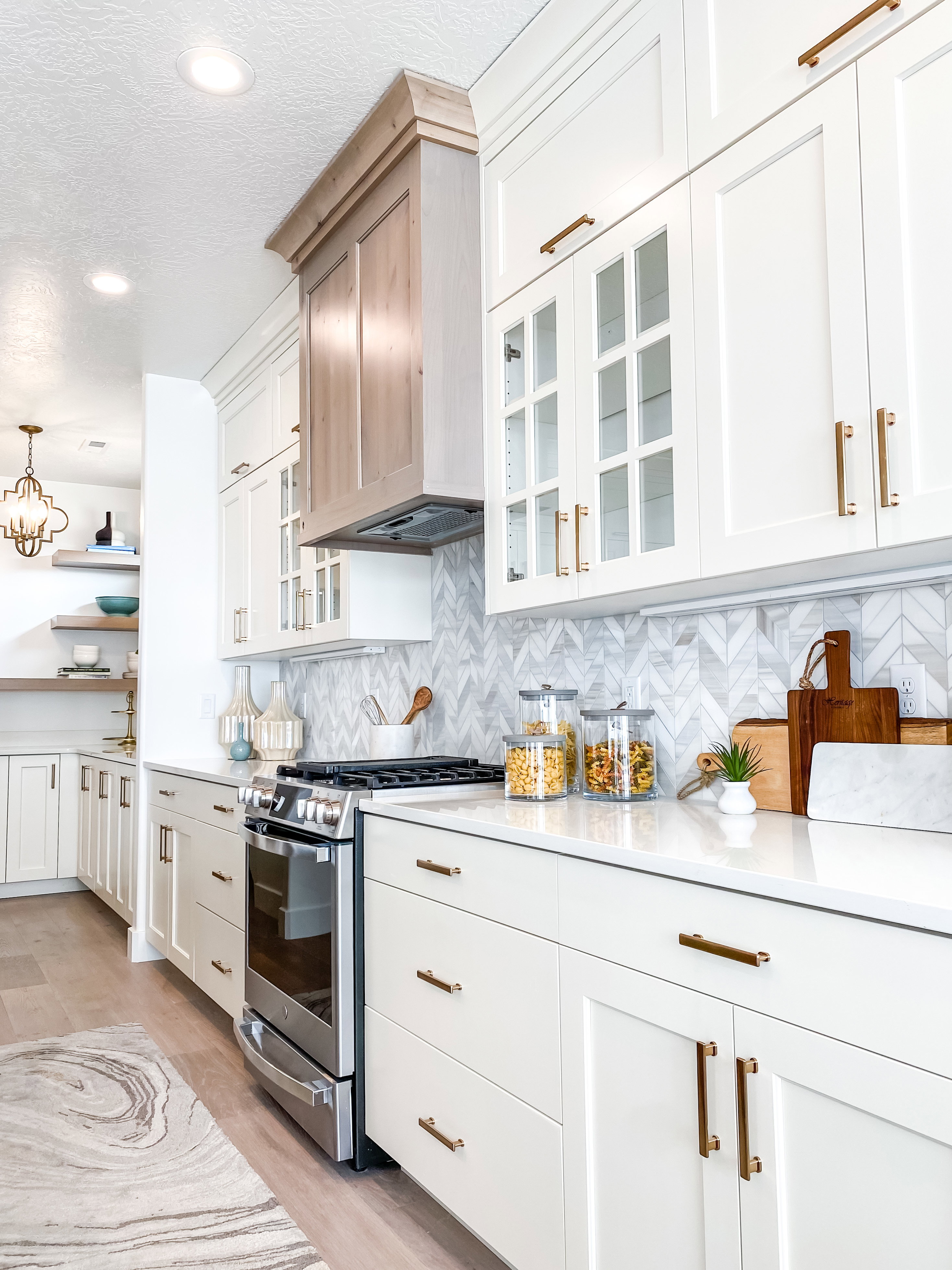 Kitchen with stainless steel range with gas stovetop, glass fronted cabinets, light stone countertops, white cabinetry, and tasteful backsplash
