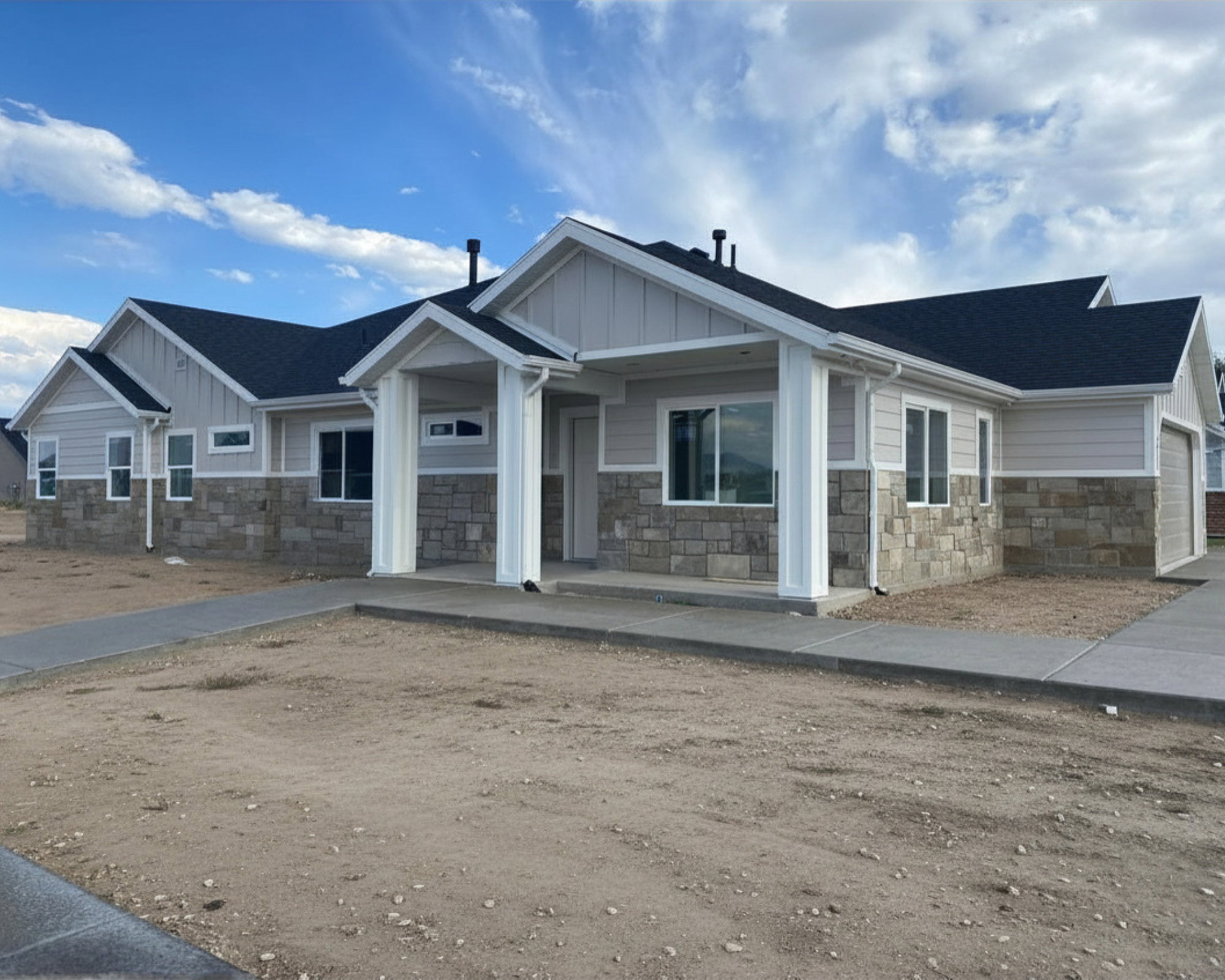 Contemporary ranch-style exterior featuring a multi-level roofline, stone and siding facade, covered entry porch with architectural columns, and multiple windows for natural light