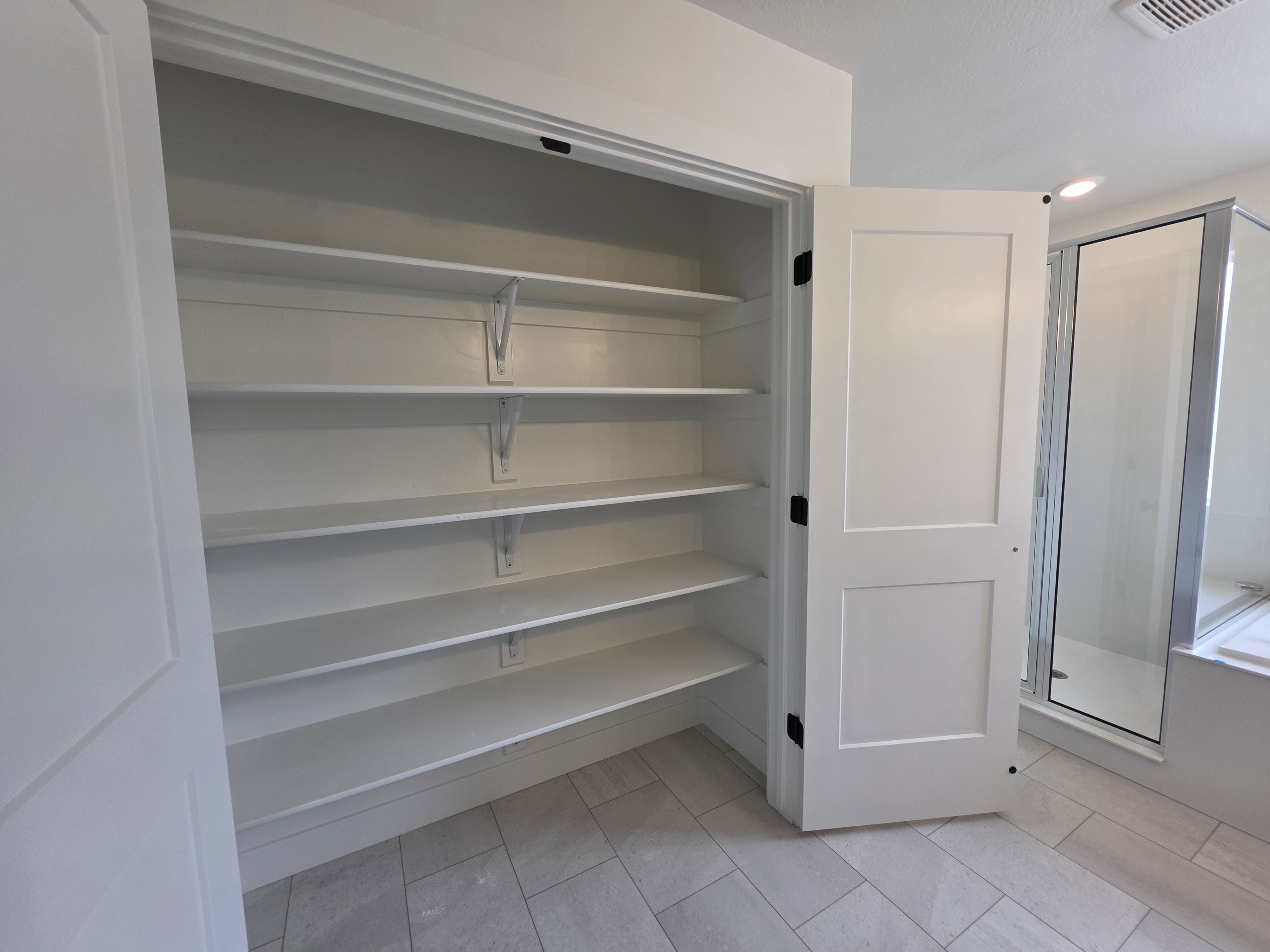Spacious built-in linen closet featuring multiple adjustable shelves, a solid core door, and black hardware