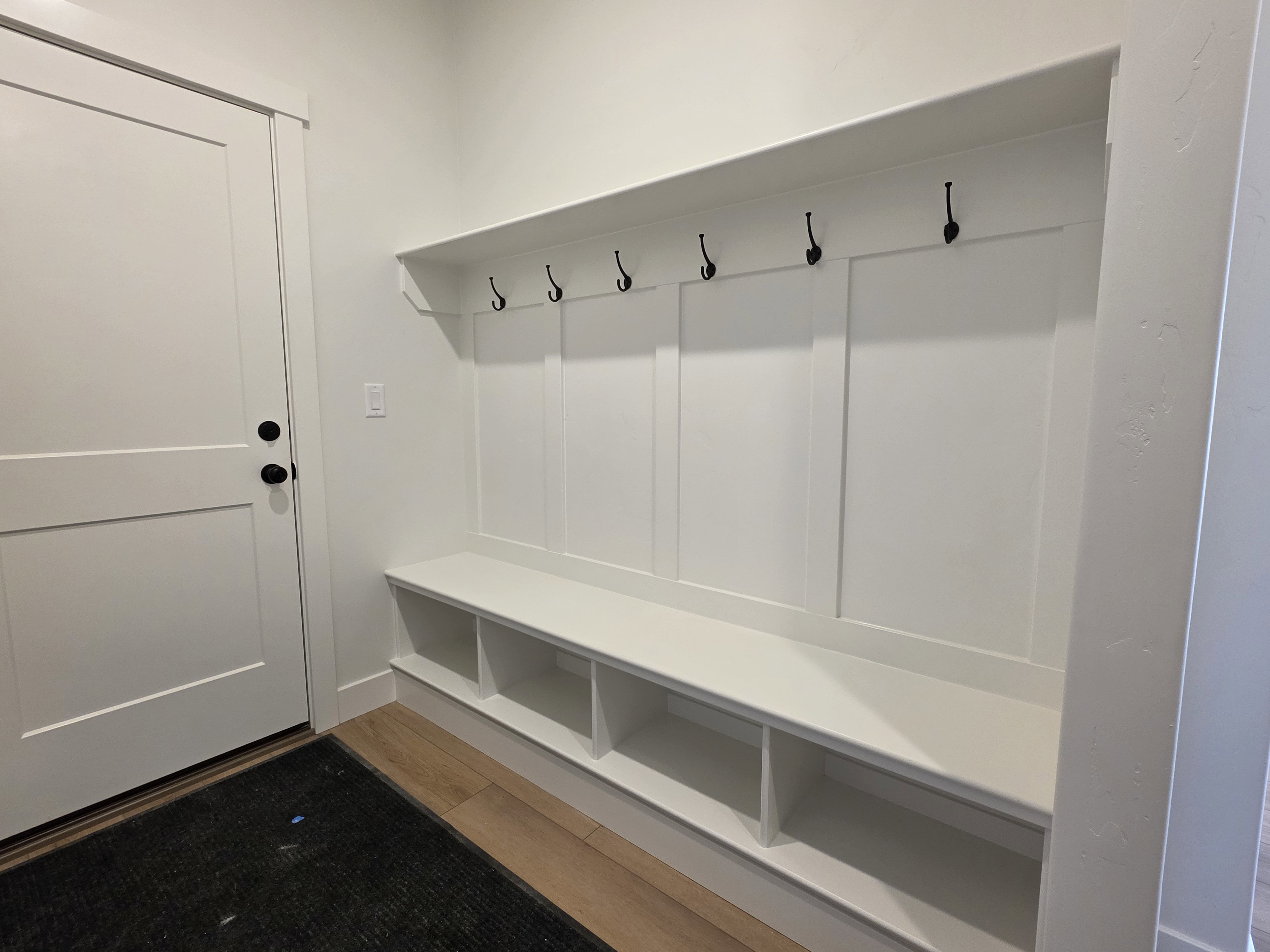 Built-in mudroom bench with cubby storage, upper shelving, and dark-finish coat hooks