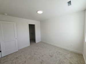 Unfurnished bedroom with a walk in closet and light colored carpet