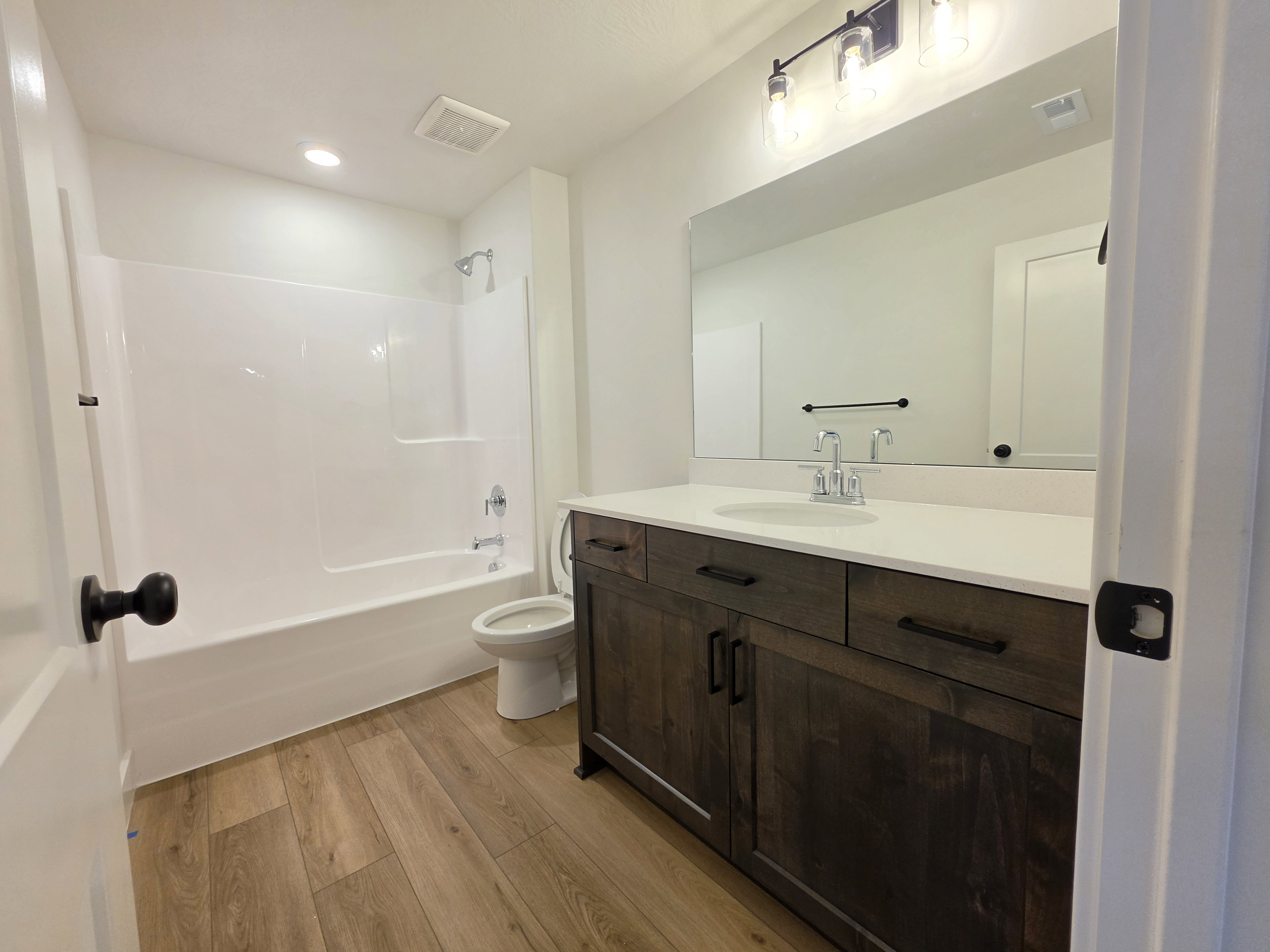Bathroom featuring a wood-finish vanity with a light-toned countertop, a full-width mirror, and a modern three-light fixture