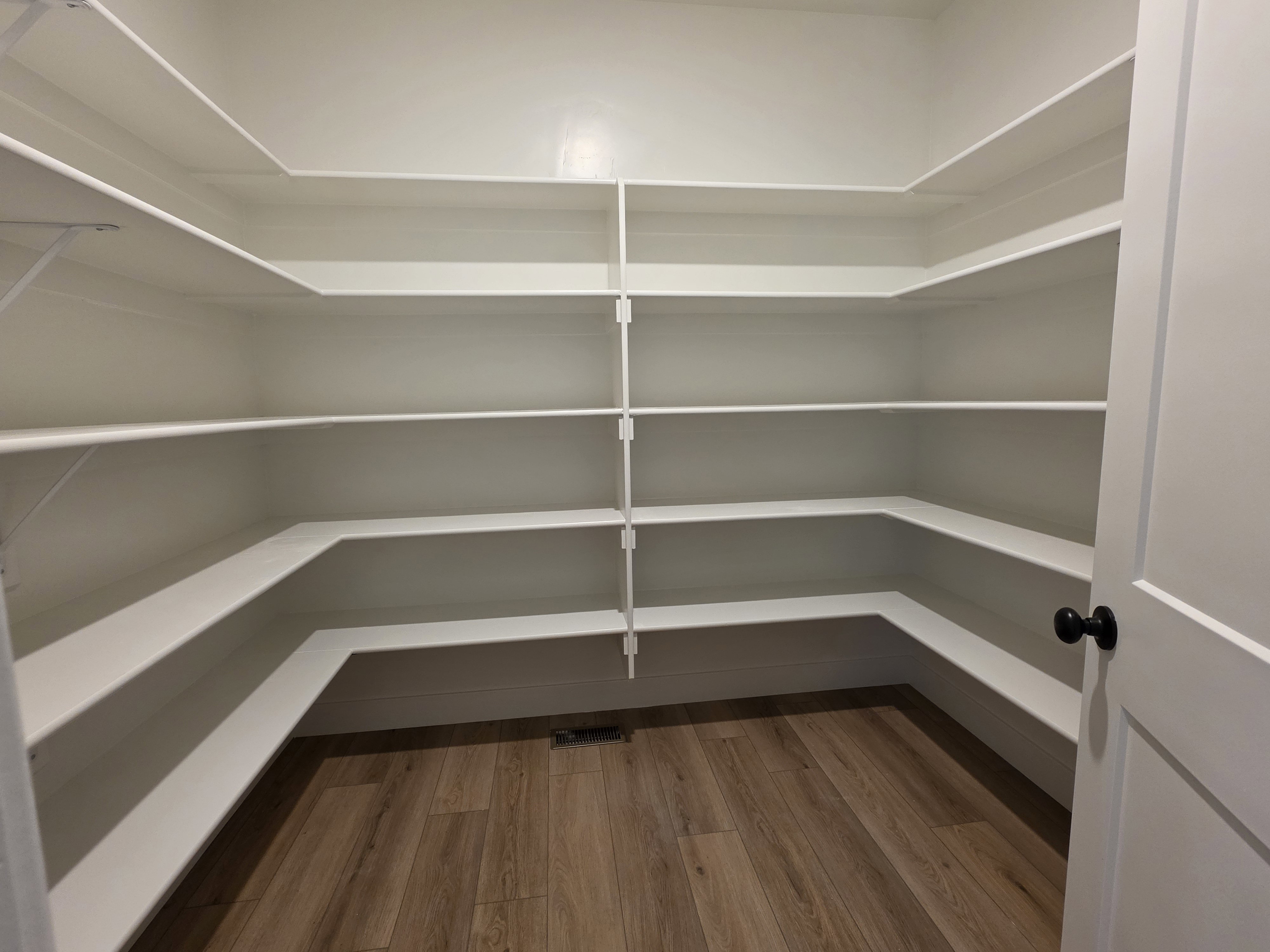 Walk-in pantry featuring extensive built-in shelving, wood-finish flooring, and a white paneled door with a matte black knob