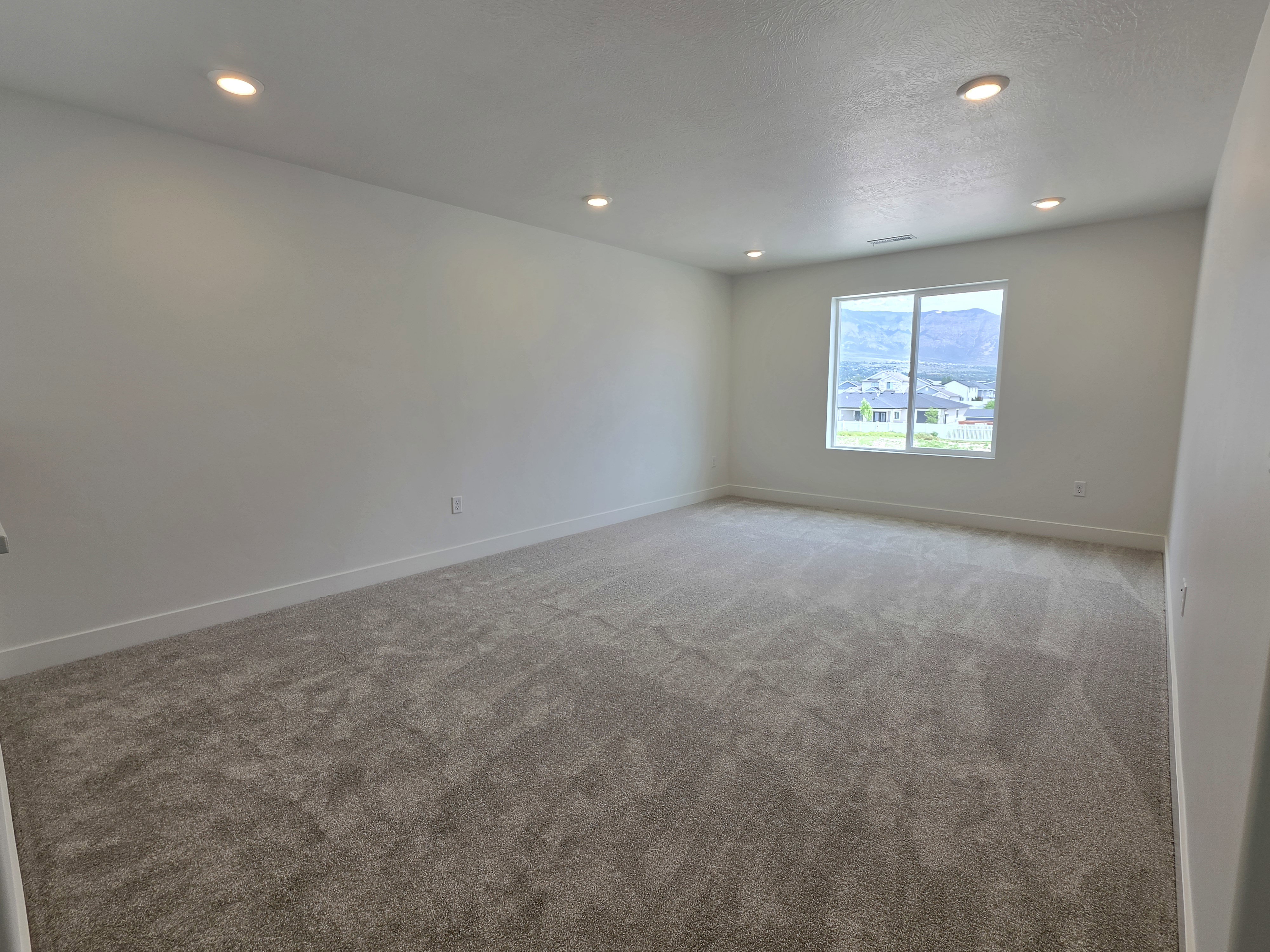 Spacious room featuring neutral carpeting, recessed ceiling lighting, a large window, a neutral color palette, and white baseboards