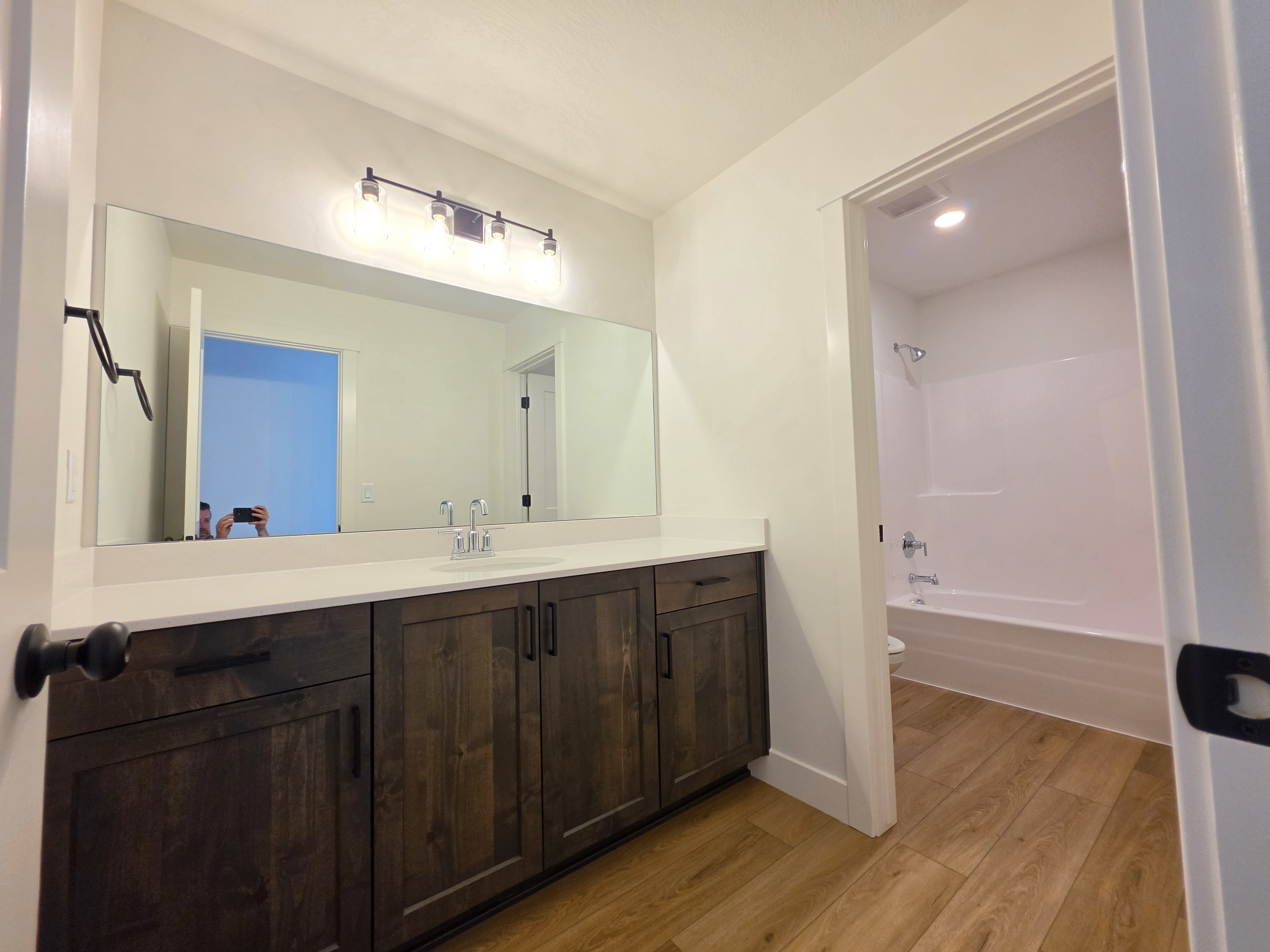 Bathroom vanity featuring a long integrated mirror, dark wood-finish cabinetry, light-toned countertop, and a single basin with a chrome faucet