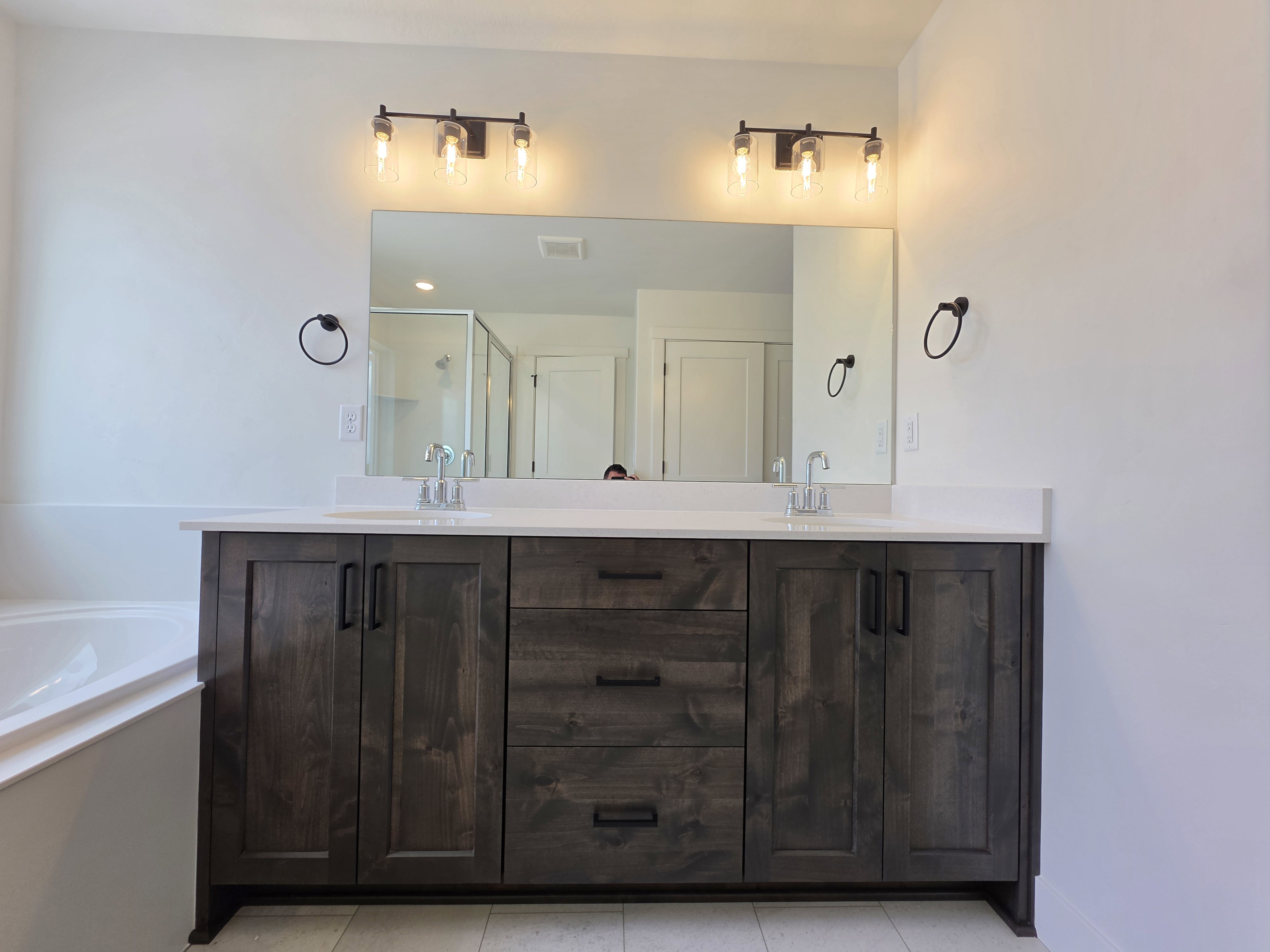 Double vanity featuring dark wood-finish cabinetry with modern black hardware, two integrated sinks, and a white countertop