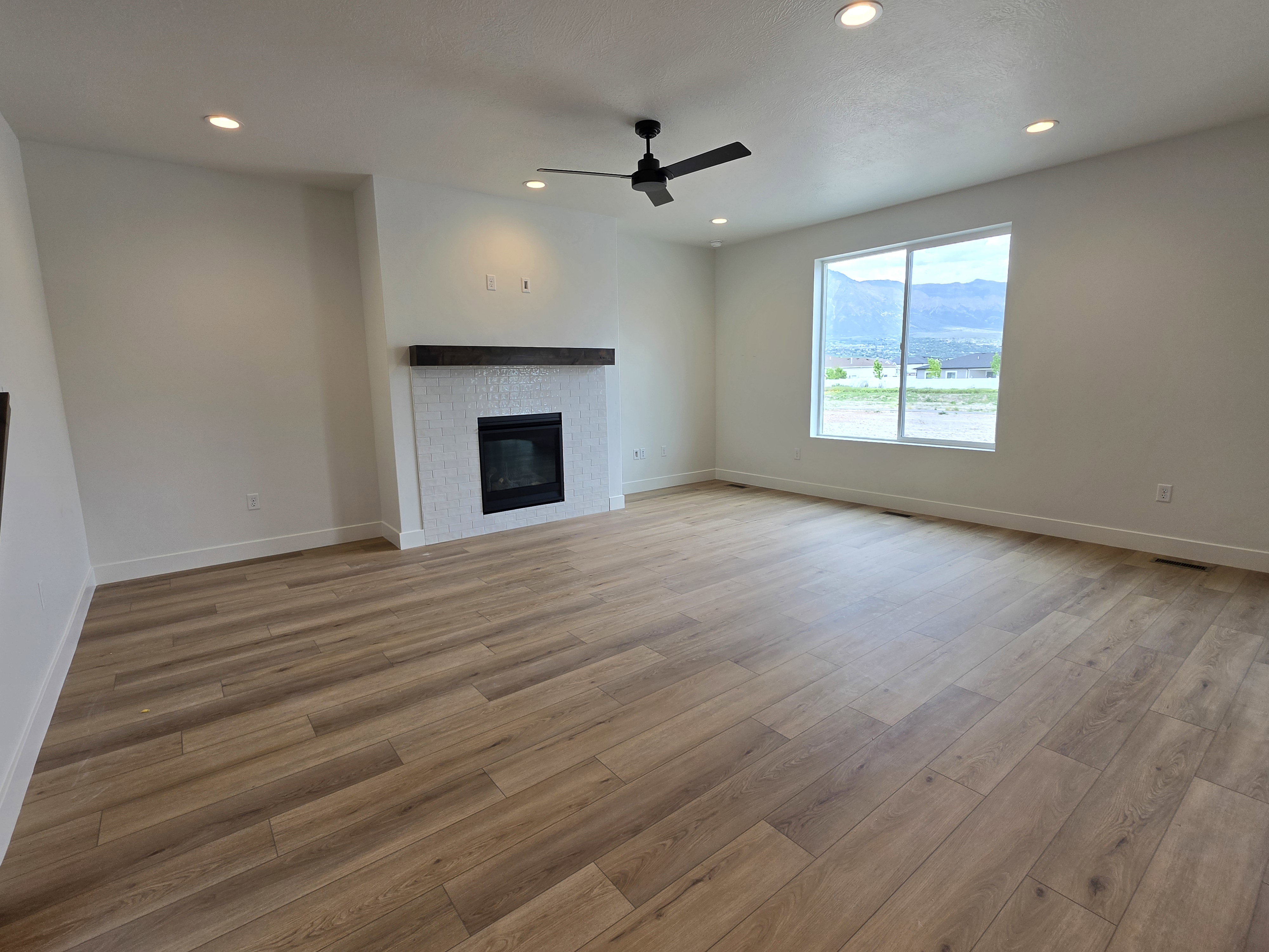 Spacious room featuring wood-finish flooring, a contemporary fireplace with white tile surround and dark wood mantel, and large windows