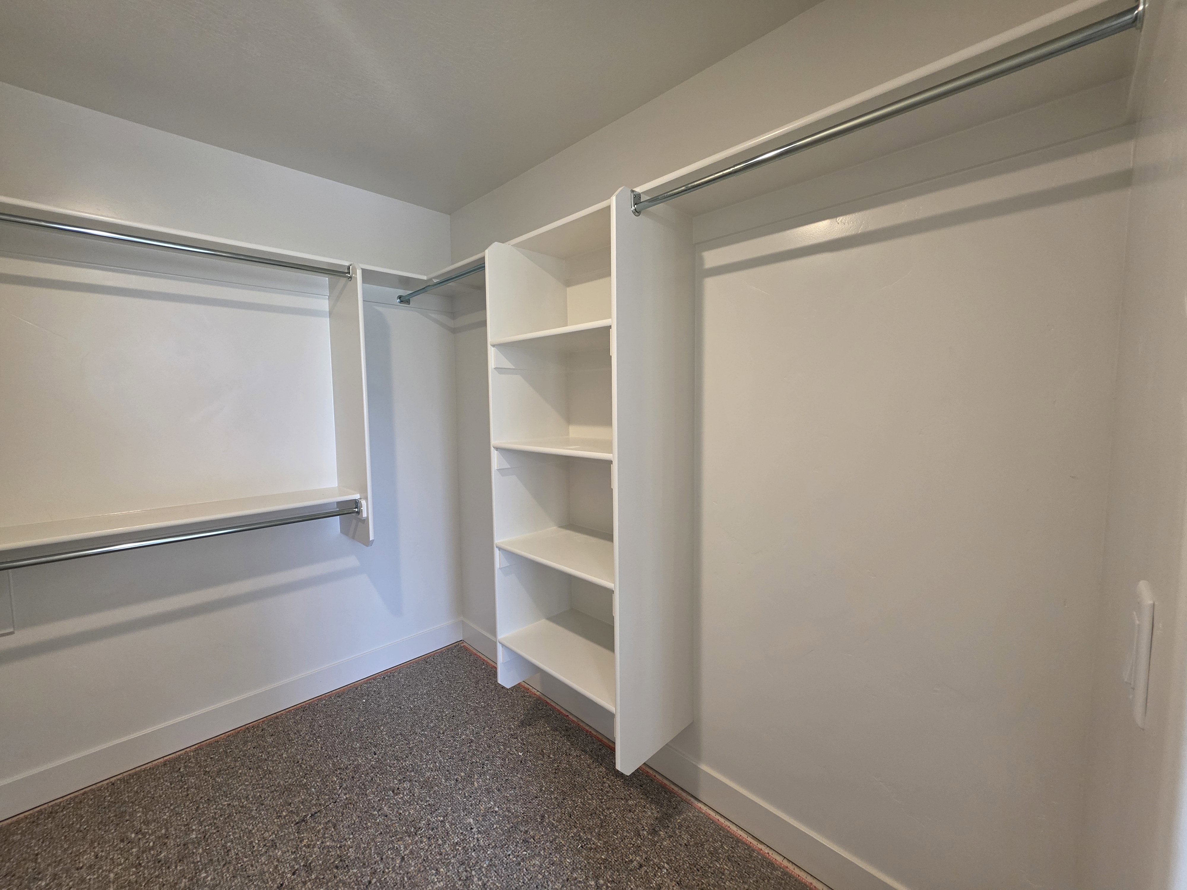 Walk-in closet with integrated shelving, multiple hanging rods, and textured carpet flooring