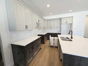 Kitchen with a center island with sink, light wood-type flooring, light stone counters, backsplash, and recessed lighting