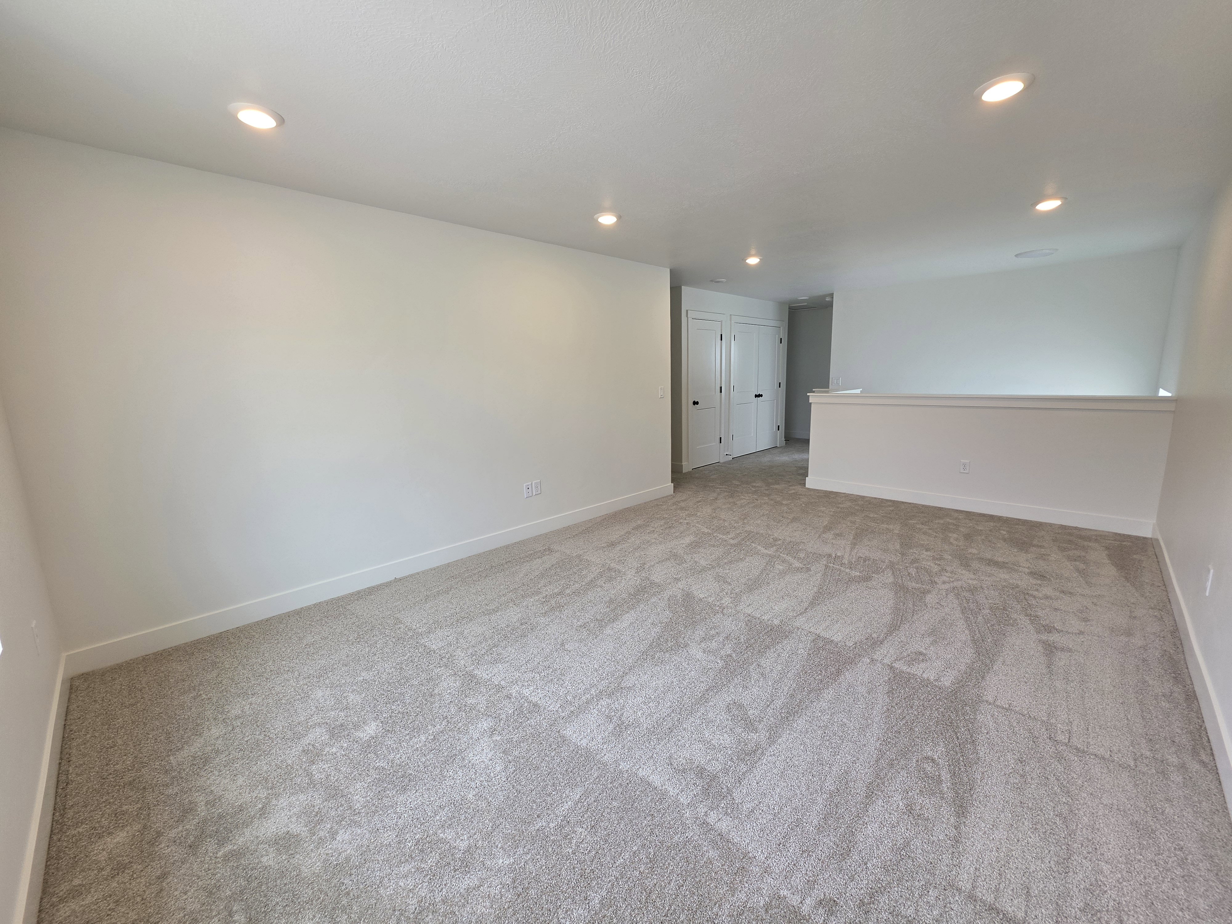 Spacious room featuring plush gray carpeting, recessed ceiling lighting, and crisp white walls