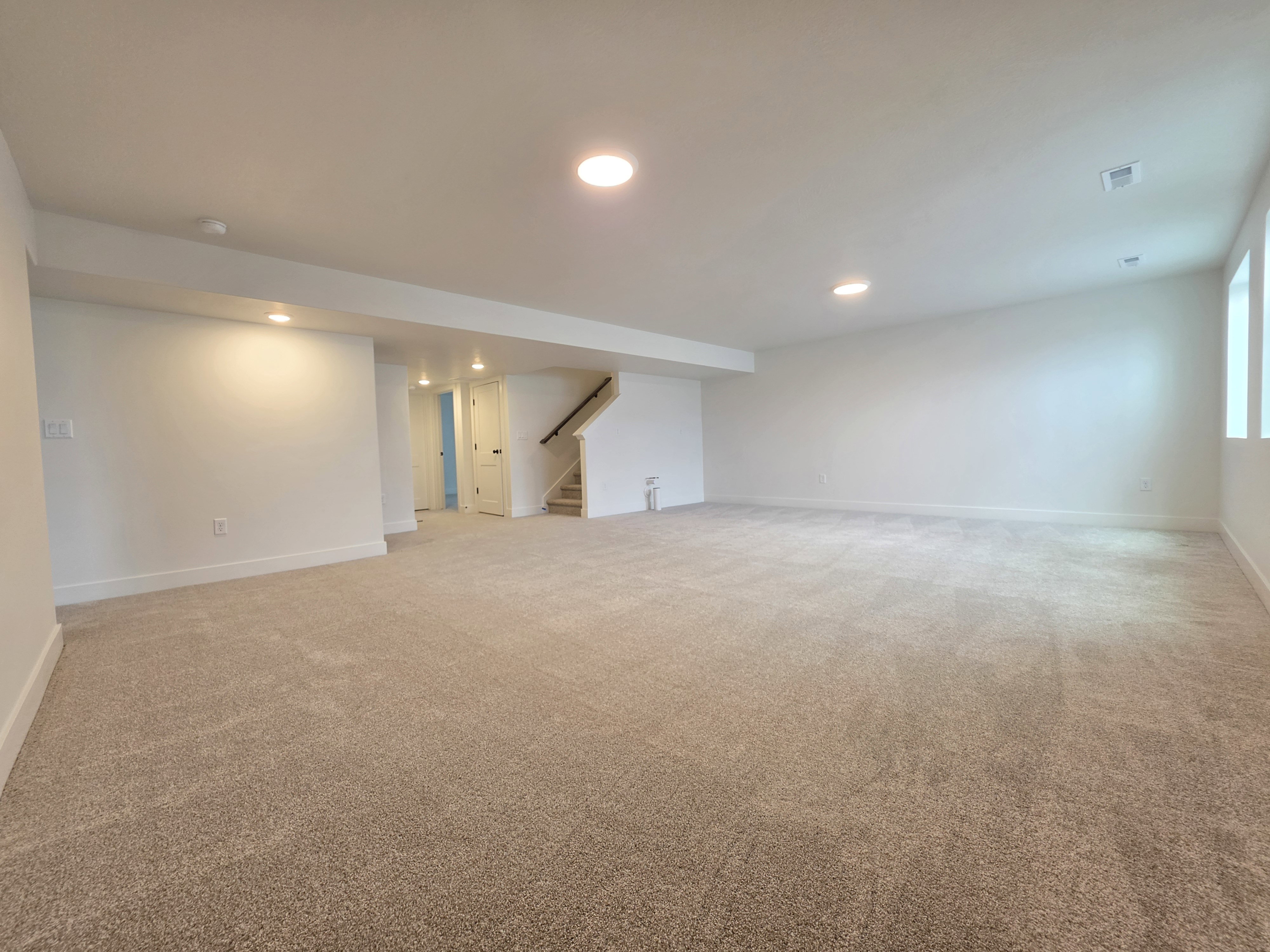 Spacious finished basement featuring recessed lighting, neutral carpeting, white trim, and a staircase with a wood handrail