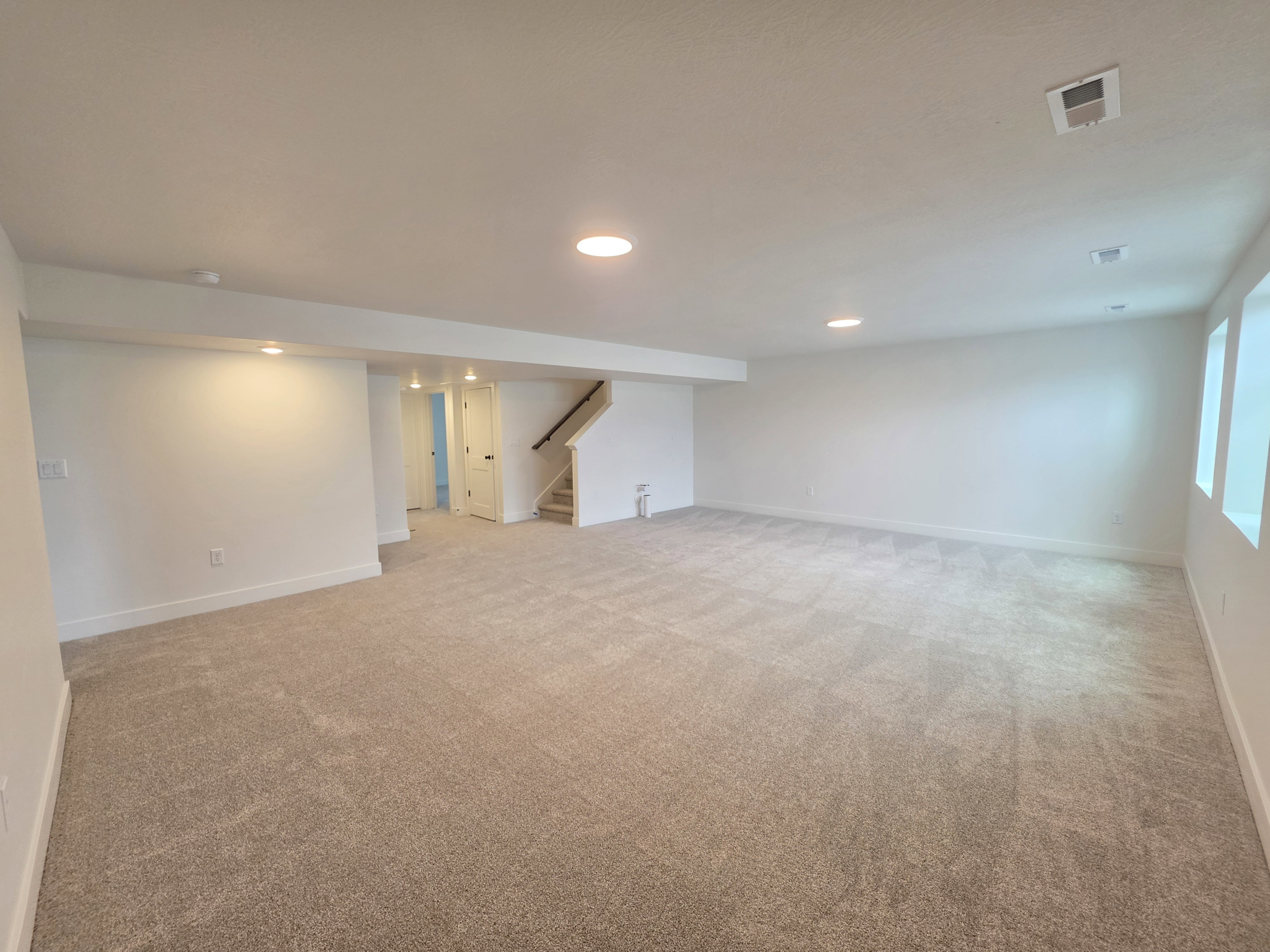 Spacious carpeted room featuring recessed lighting, white walls, and a staircase with a dark wood handrail