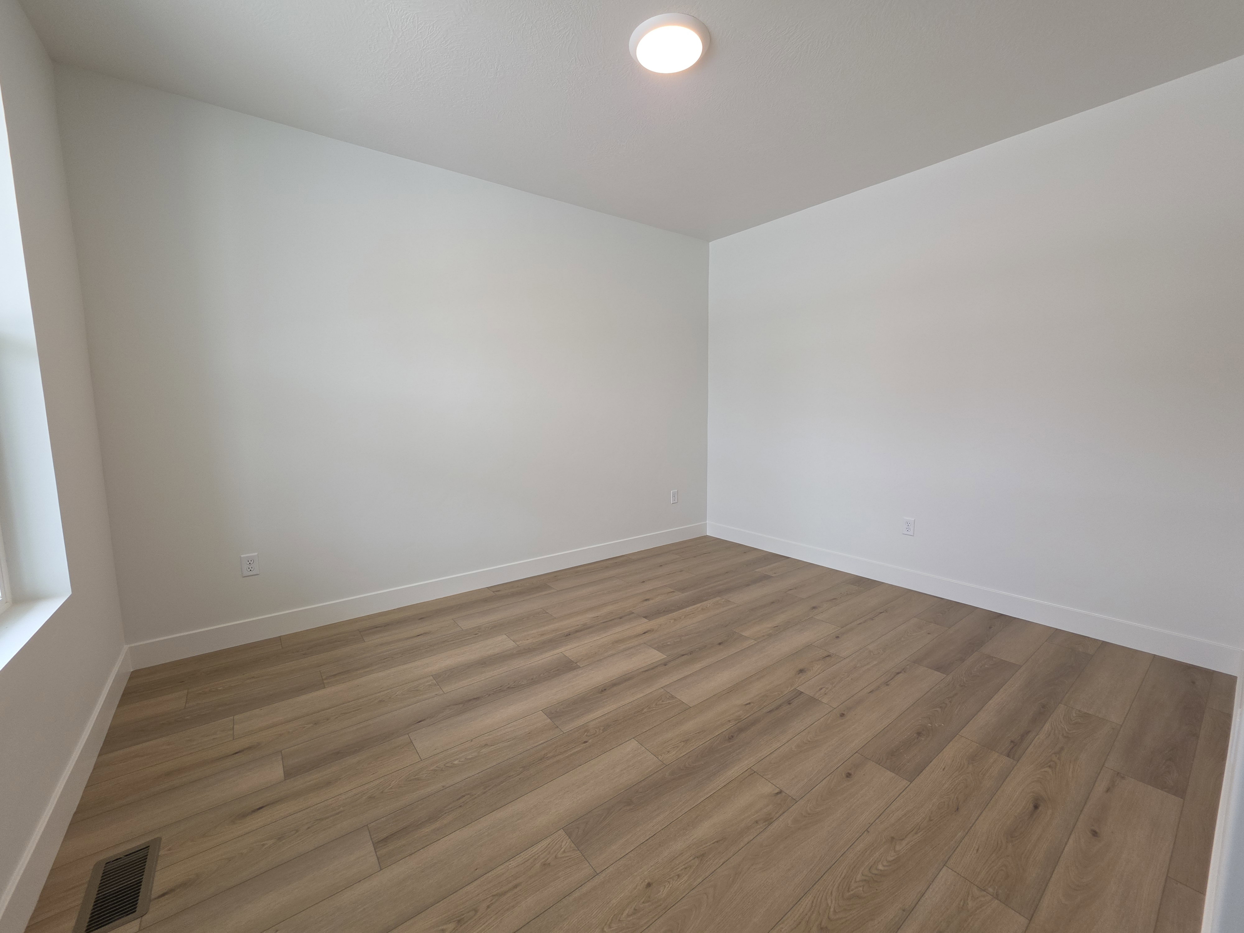 Spacious room featuring wood-finish flooring, crisp white walls, recessed ceiling lighting, and a prominent window