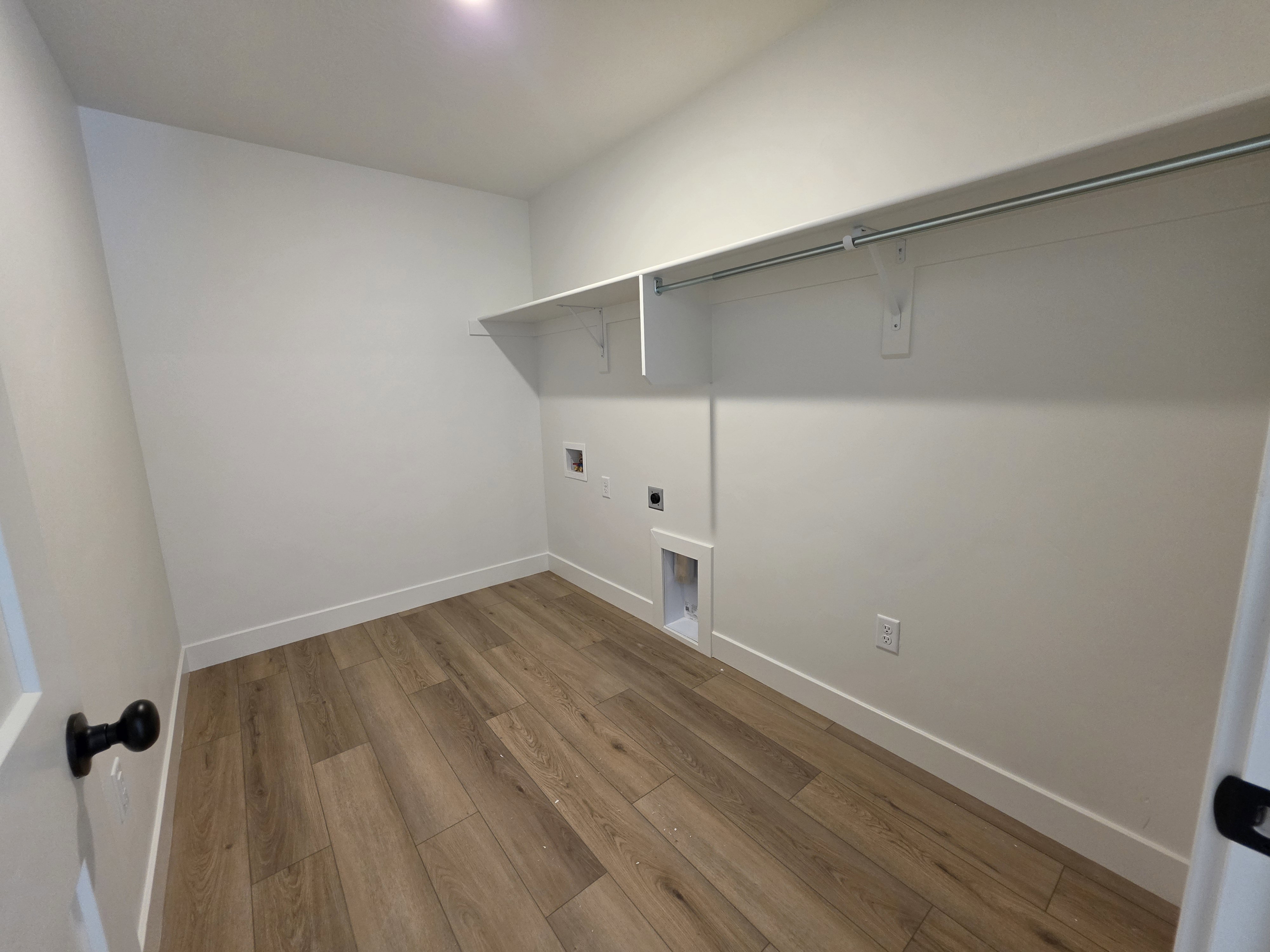Functional utility space featuring wood-finish flooring, white walls, and built-in shelving with a hanging rod