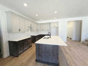 Kitchen featuring an island with sink, light wood-style floors, light stone countertops, recessed lighting, and backsplash