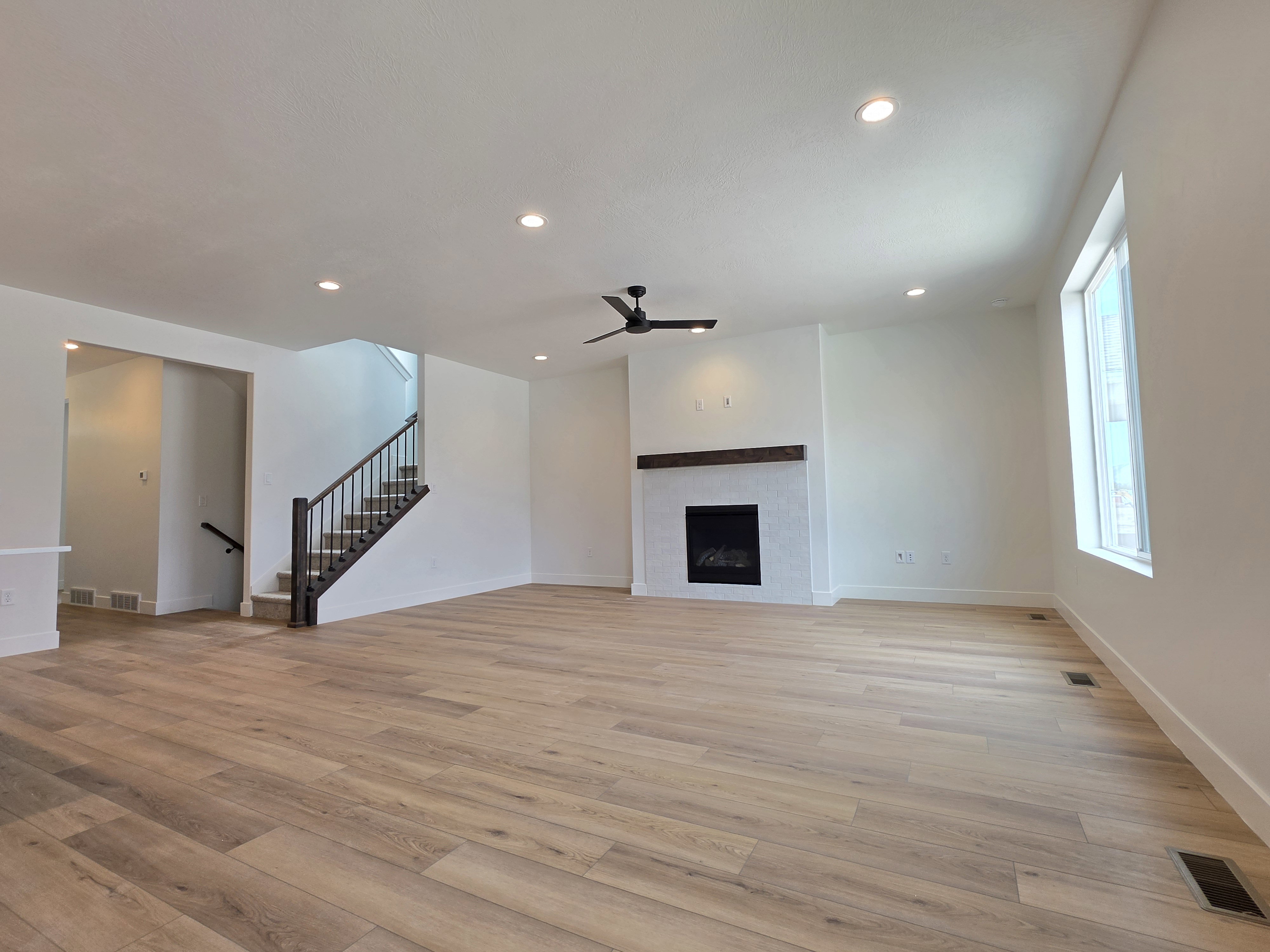 Spacious living area featuring wood-finish flooring, a white-tiled fireplace with a wood mantle, a ceiling fan, and recessed lighting