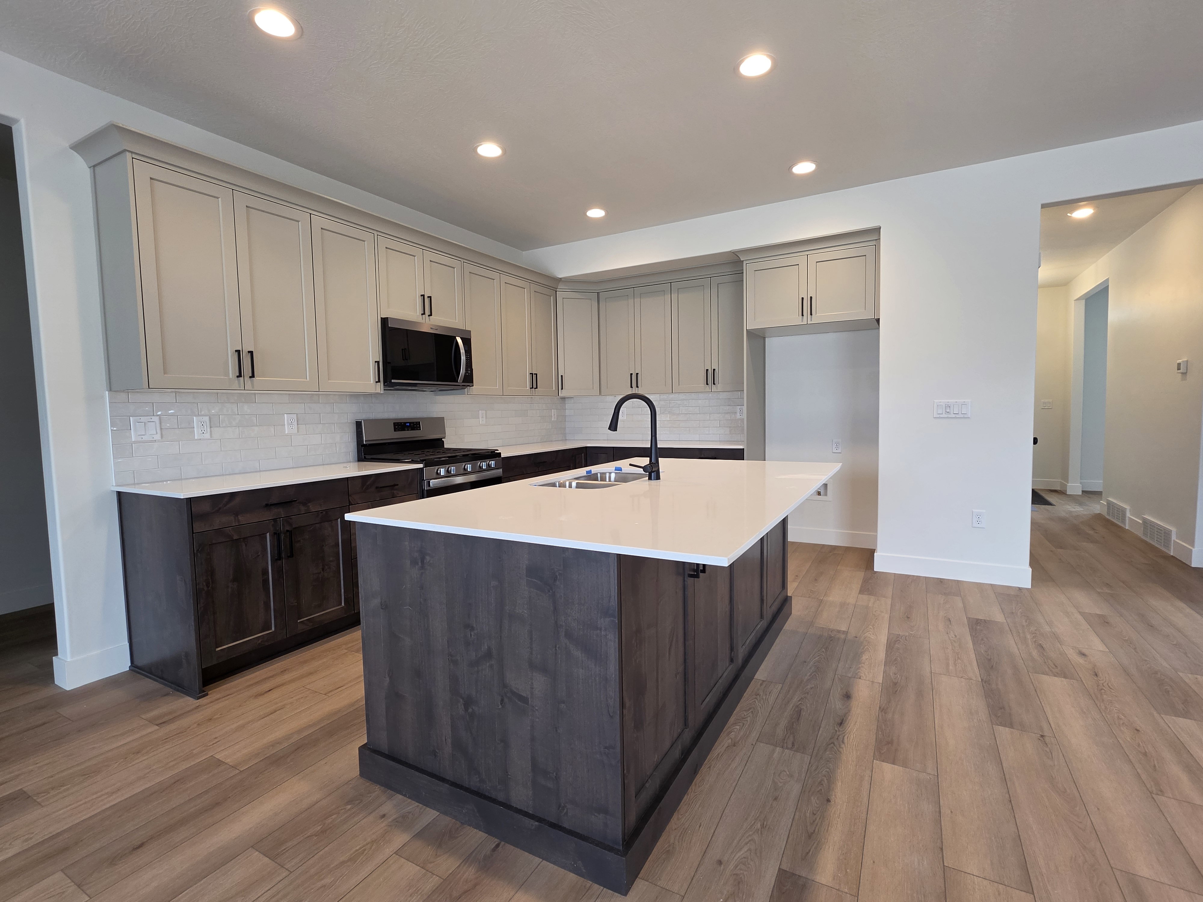 Contemporary kitchen featuring two-tone cabinetry, a central island with a sink and matte black faucet, stainless steel microwave, and wood-finish flooring