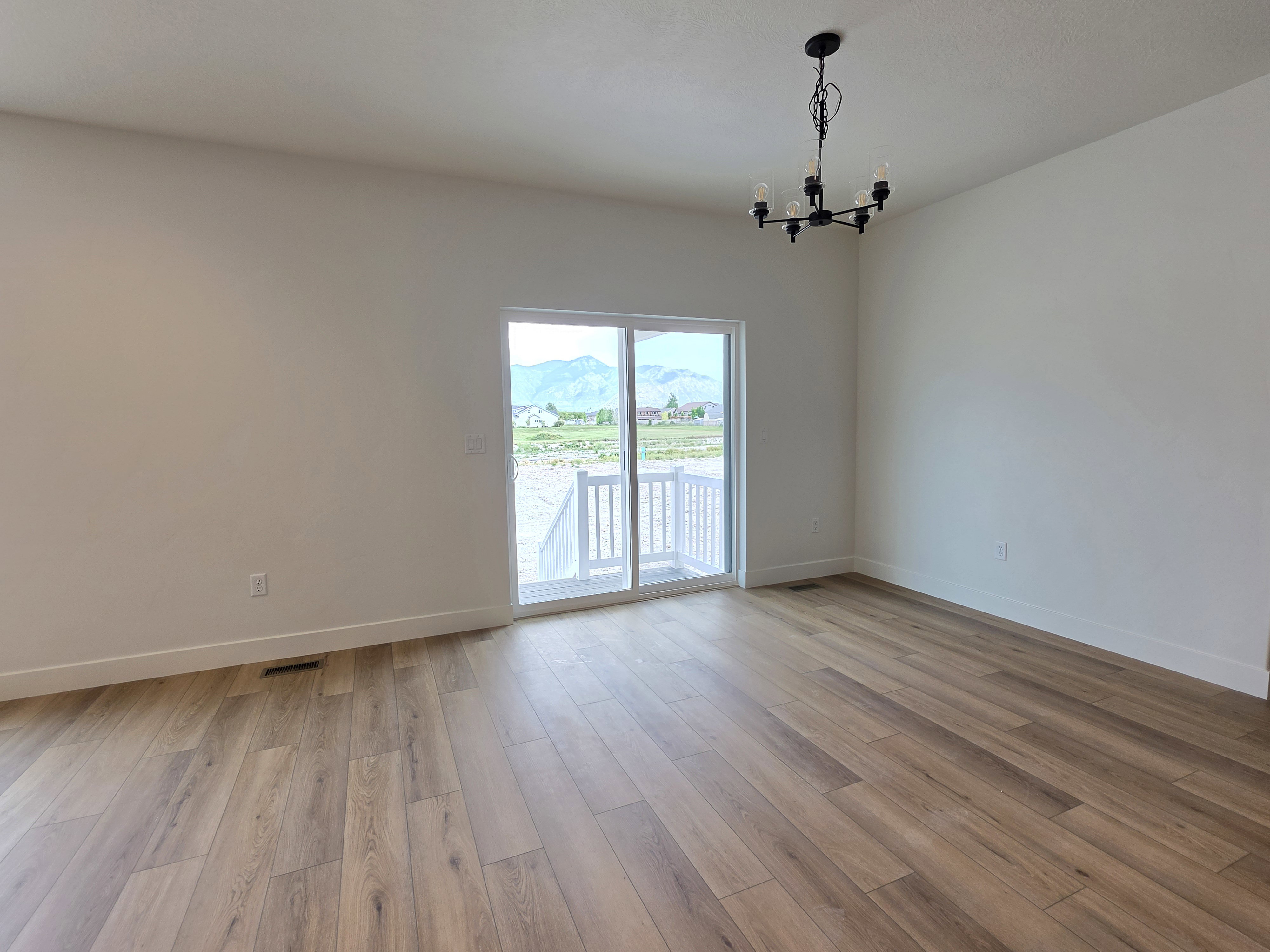 Spacious room featuring wood-finish flooring, white baseboards, and a contemporary black chandelier