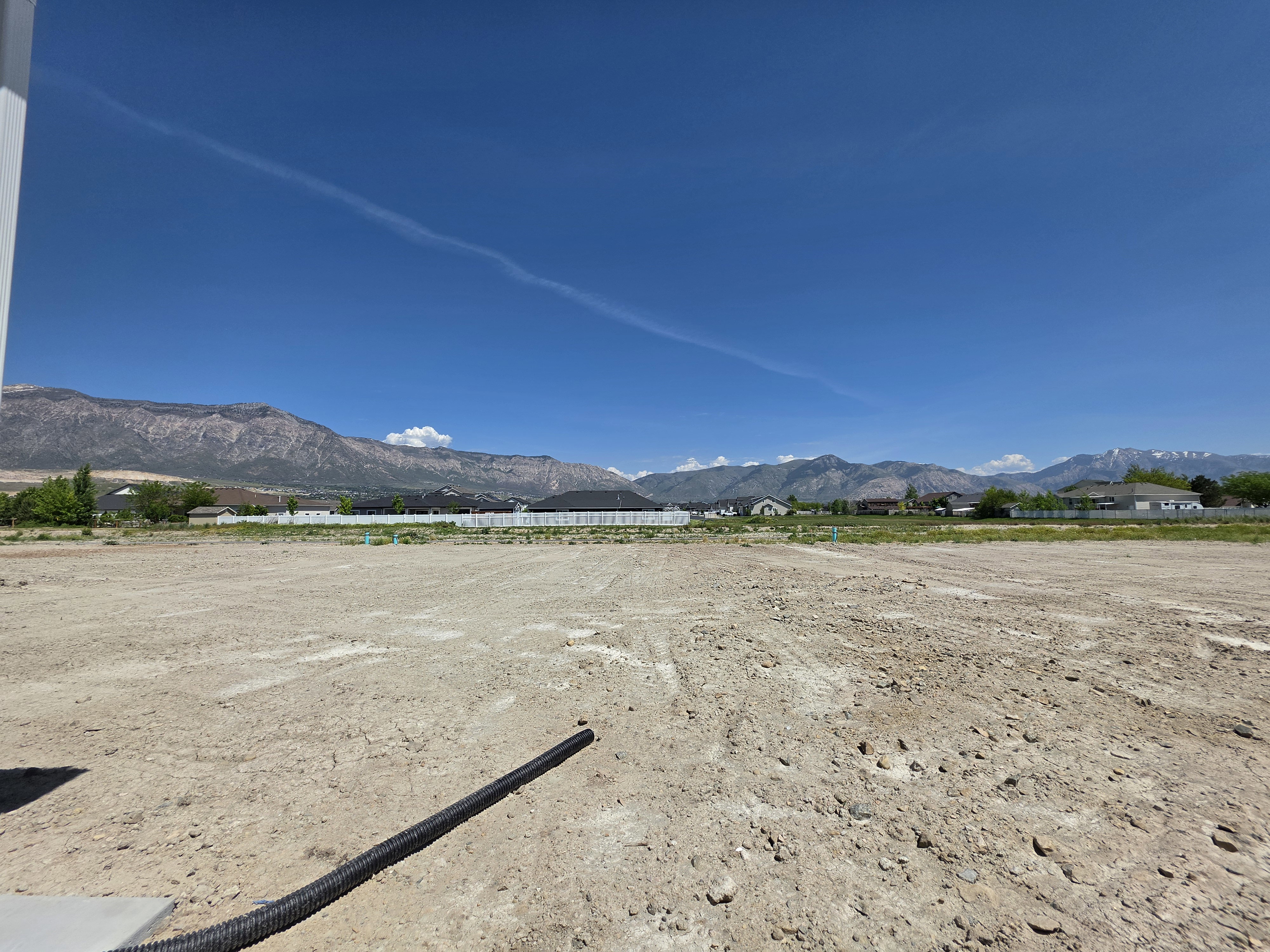 Expansive cleared lot with a visible drainage pipe, featuring a backdrop of distant mountains