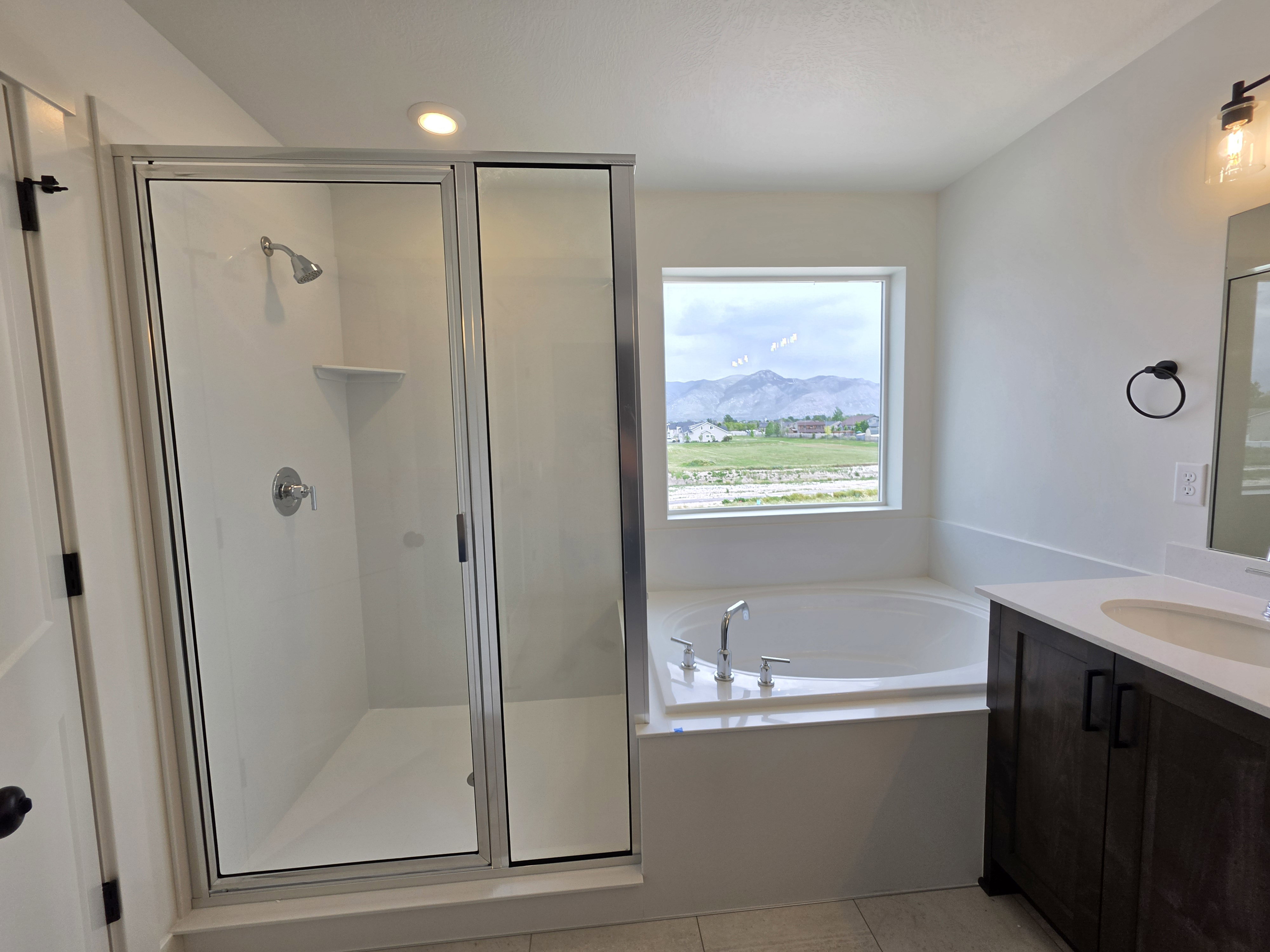 Bathroom featuring a glass-enclosed shower, built-in soaking tub with chrome fixtures, wood-finish vanity with an undermount sink, and a framed mirror