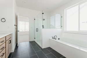 Full bath featuring a shower stall, vanity, a garden tub, and dark tile patterned flooring