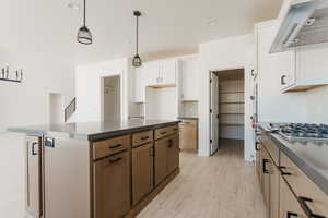 Dual tone kitchen with dark countertops, dual tone cabinetry, range hood, backsplash, and light wood-type flooring