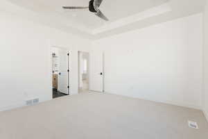 Unfurnished bedroom with dark carpet, a raised ceiling, a ceiling fan, and connected bathroom