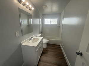 Full bath with a textured ceiling, vanity, dark wood-style floors, and  shower combination