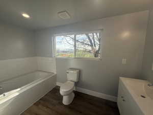 Bathroom featuring vanity, a bath, dark wood-style flooring, and recessed lighting