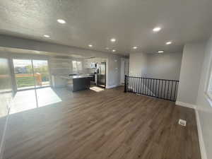 Two tone kitchen featuring open floor plan, recessed lighting, stainless steel appliances, dark wood-style flooring, and a center island