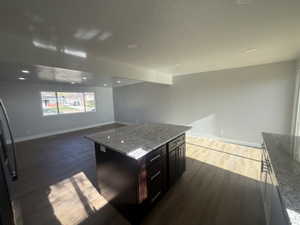 Kitchen with light stone counters, a kitchen island, freestanding refrigerator, dark wood finished floors, and open floor plan