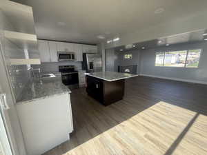 Dual tone kitchen featuring light stone countertops, stainless steel appliances, open shelves, a center island, and light wood-type flooring