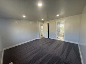 Unfurnished bedroom with recessed lighting, dark colored carpet, and ensuite bath