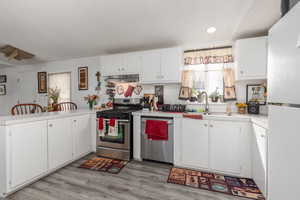 Kitchen with stainless steel appliances, a peninsula, light countertops, white cabinetry, and light wood-style floors