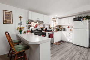 Kitchen with a kitchen bar, stainless steel appliances, a peninsula, white cabinetry, and a textured ceiling