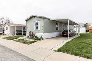 Manufactured / mobile home with an attached carport, concrete driveway, and a front yard