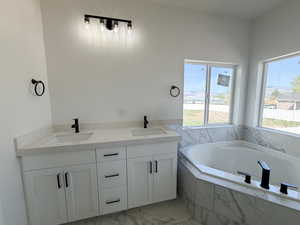 Full bathroom featuring double vanity, a garden tub, and light marble finish floors