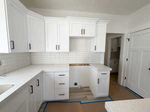 Kitchen with white cabinetry, decorative backsplash, and wood finished floors