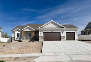 Craftsman house with covered porch, board and batten siding, an attached garage, stone siding, and driveway