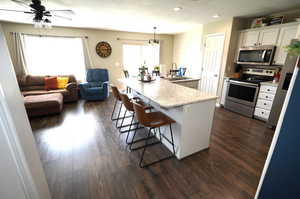 Kitchen with stainless steel appliances, a kitchen bar, a center island with sink, dark wood-type flooring, and a textured ceiling