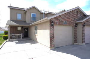 Traditional home featuring stucco siding, brick siding, roof with shingles, a garage, and driveway
