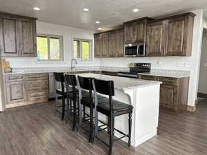 Kitchen with stainless steel appliances, a kitchen breakfast bar, light stone counters, dark wood finished floors, and dark wood finish cabinetry