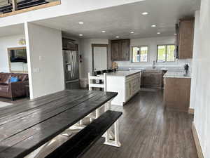 Two tone kitchen with light stone countertops, stainless steel appliances, dark wood-style floors, recessed lighting, and a kitchen island
