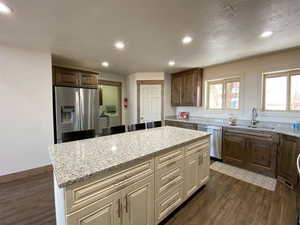Kitchen featuring stainless steel appliances, dark wood-style floors, light stone counters, recessed lighting, and two tone cabinetry