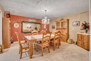 Dining area with light carpet, suspended lighting, a textured ceiling, and a textured wall