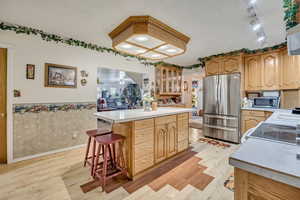 Kitchen featuring light countertops, a wainscoted wall, glass insert cabinets, and a center island